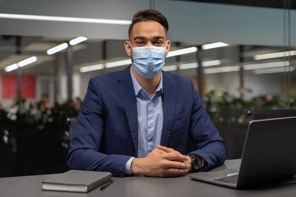 Gerente árabe em máscara facial sentado na mesa de trabalho com computador — Fotografia de Stock