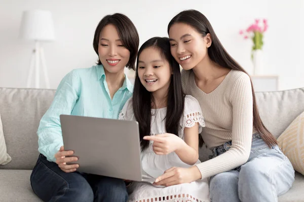 Sorrindo menina asiática com sua mãe e avó assistindo vídeo, pesquisando internet no laptop na sala de estar — Fotografia de Stock
