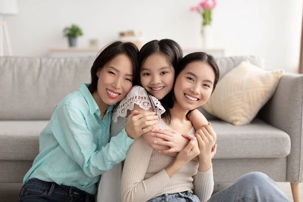 Giovane donna asiatica con la sua figlia carina e madre matura che abbraccia e sorride alla fotocamera al chiuso — Foto Stock