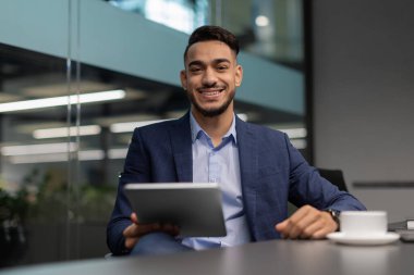 Dijital tablet kullanarak ofiste çalışan neşeli orta doğulu işadamı