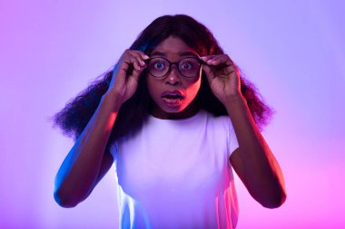 Duygusal genç siyah kadın gözlüğe dokunuyor, neon ışıkta kamera iyon şokuna bakıyor.