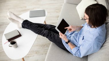 Adam boş ekranlı modern dijital tablet kullanıyor, kanepeye yaslanıyor, mobil uygulama ya da web sitesi kullanıyor,