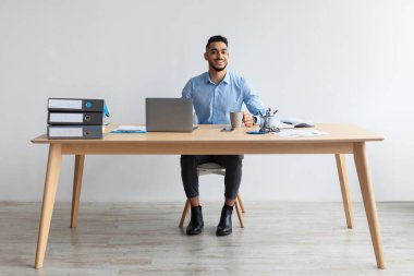 Laptop kullanan ve poz veren gülümseyen bir Arap portresi.