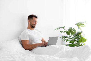 Beyaz tişörtlü yakışıklı beyaz adam bilgisayarda blog yazmakla meşgul.