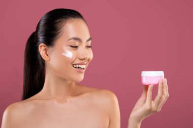 Çekici çıplak Asyalı kadın elinde kremalı pembe kavanoz tutuyor.