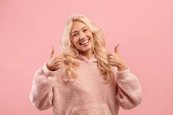 A mí me gusta. Retrato de mujer rubia excitada mostrando los pulgares hacia arriba y sonriendo a la cámara sobre fondo de estudio rosa — Foto de Stock