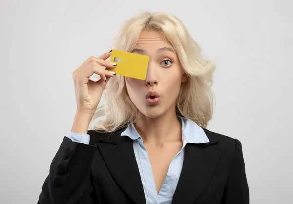 Überraschte erfolgreiche Geschäftsfrau bedeckt Auge mit EC-Kreditkarte, posiert über hellgrauem Studiohintergrund — Stockfoto