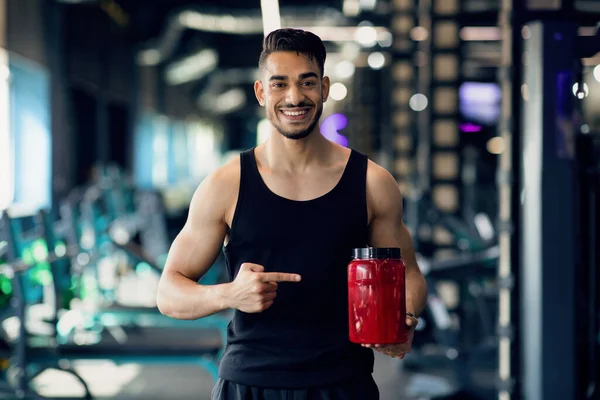 Musculação Nutrição. Desportista árabe feliz apontando para Contrainer vermelho com soro de leite em pó — Fotografia de Stock
