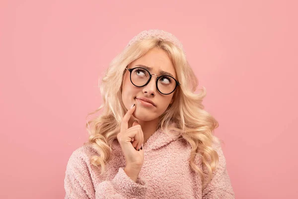 Портрет стомленої блондинки, яка торкається підборіддя і дивиться вбік, позує на рожевому студійному фоні — стокове фото
