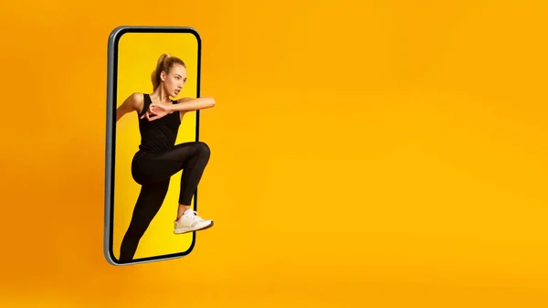 Athletische Dame springt von riesigem Smartphone-Bildschirm, gelber Hintergrund — Stockfoto