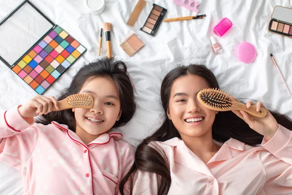 Felice soddisfatto giovane ragazza asiatica femminile e adolescente, vicino occhio con pettine, sdraiarsi sul letto con cosmetici in camera da letto — Foto Stock