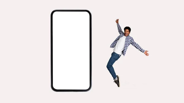 快乐黑人男子跳跃靠近智能手机空屏幕，灰色背景 — 图库照片