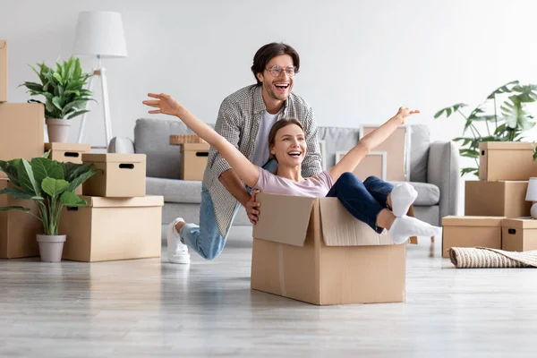 Веселий білий чоловік відчуває себе грайливо з щасливою дружиною катається в картонних коробках під час переїзду в новий будинок — стокове фото