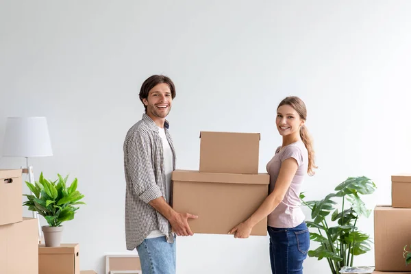 Happy young european lady and guy carry cardboard box with belongings in empty room interior — Stock Photo, Image