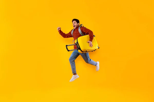 Emotionele Man Tourist Jumping Carrying Suitcase Over Yellow Studio Achtergrond — Stockfoto