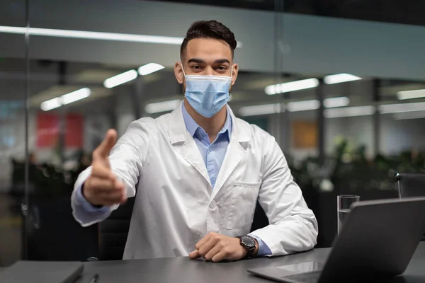 Médico em máscara facial sentado na mesa de trabalho, saudação paciente — Fotografia de Stock