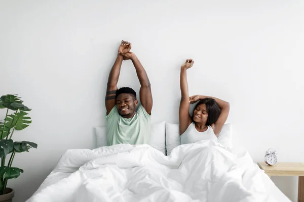 Vidám, ezeréves afro-amerikai feleség és férj felébredt alvás után, testeket nyújtva az ágyon. — Stock Fotó