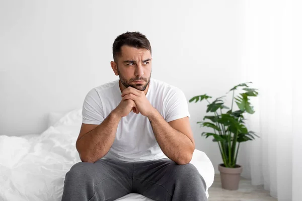 Depresión infeliz europeo millennial hombre en camiseta blanca sufre de problemas se sienta en la cama en el dormitorio — Foto de Stock