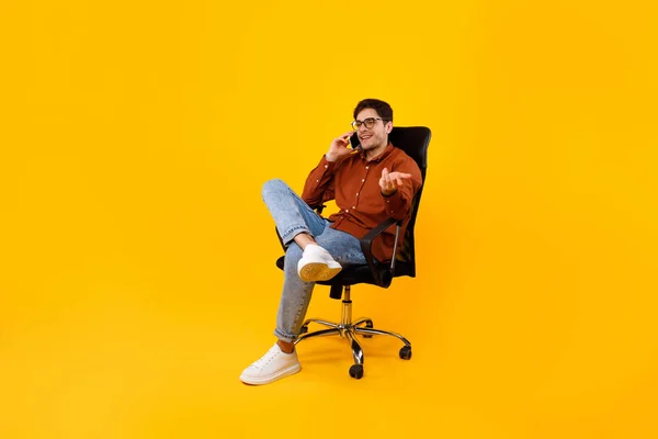 Telefonda konuşan adam, sarı arka planda oturan sandalyede oturuyor. — Stok fotoğraf
