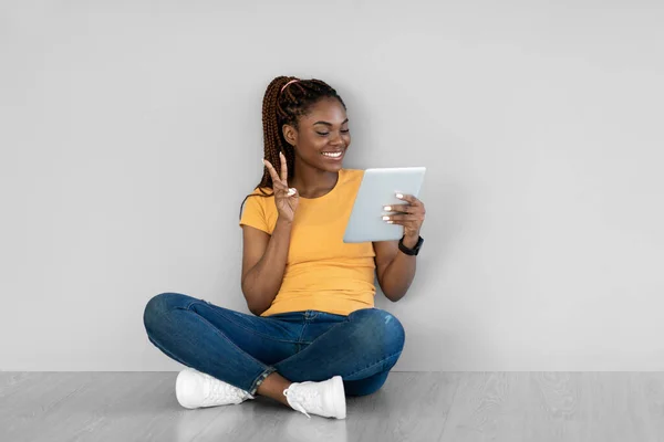 Online kommunikáció. Bájos fiatal fekete nő videó chat tabletta pc, mutatja a béke gesztus webkamera — Stock Fotó
