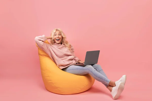 Ενθουσιασμένη νεαρή κυρία κάθεται στην καρέκλα με το laptop, φωνάζοντας wow, γιορτάζει μεγάλη είδηση, ροζ φόντο — Φωτογραφία Αρχείου