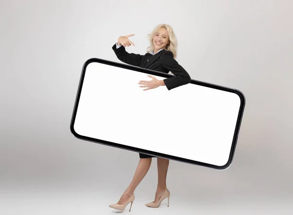 Longitud de cuerpo completo disparo de mujer de negocios feliz llevando un gran teléfono inteligente con pantalla en blanco y apuntando a la pantalla del gadget — Foto de Stock