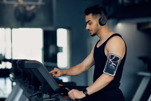 Fitnesstraining. Junger Mann aus dem Nahen Osten trainiert mit drahtlosen Kopfhörern auf Laufband — Stockfoto