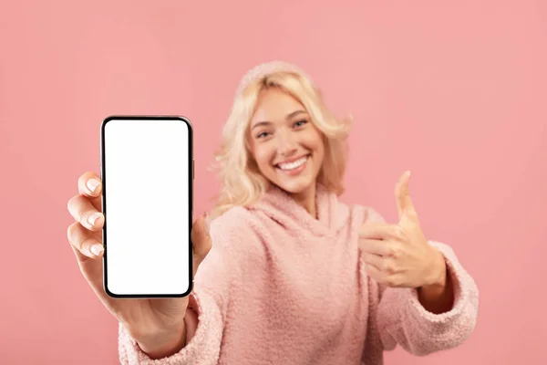 Красивая юная леди показывает смартфон с пустым экраном и большим пальцем вверх, сотовый телефон с пустым дисплеем, макет — стоковое фото