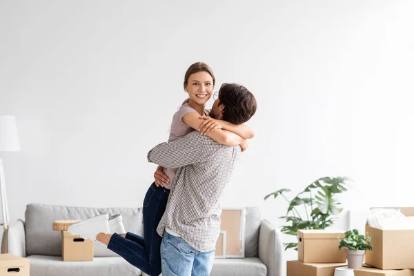 Feliz hombre caucásico abraza y levanta a su esposa celebrando la compra de nuevo apartamento, pareja divertirse juntos —  Fotos de Stock