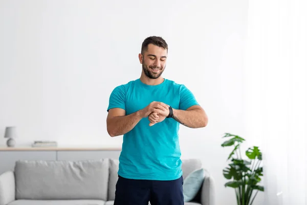 Feliz atleta europeo millennial chico feliz en uniforme comprobar el pulso en el rastreador de fitness en el interior de la sala de estar — Foto de Stock