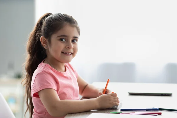 Hermosa niña sentada en la mesa y dibujando con lápices de colores —  Fotos de Stock