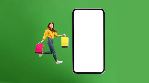 Podekscytowana kobieta zakupoholiczka skacze do ogromnego smartfona na zielonym tle — Zdjęcie stockowe
