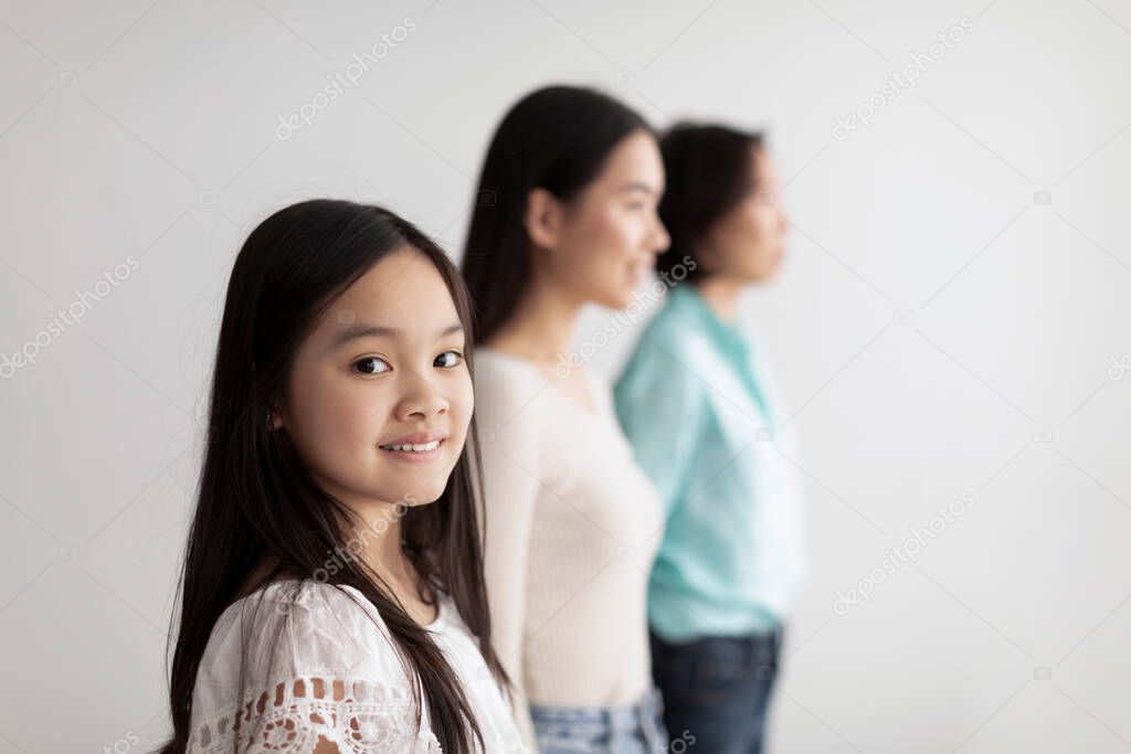 Cheerful little Asian girl with her mother and grandmother posing on white studio background, copy space