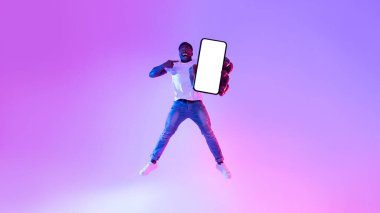 Yakışıklı genç siyah adam beyaz ekranlı akıllı telefonu işaret ediyor, havaya zıplıyor, modellik için yer sunuyor.