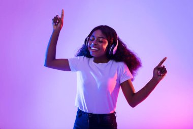 Neşeli, kulaklıklı, müzik dinleyen ve neon ışıkta dans eden Afro-Amerikan kadın.