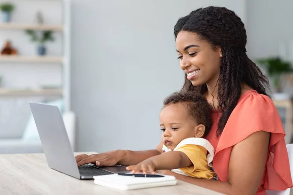 Портрет черной женщины с ребенком на руках с помощью ноутбука дома — стоковое фото