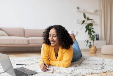 Bilgisayarı kullanan, çalışan ya da internetten okuyan, evde web sitesi kuran Afrikalı Amerikalı bir kadın.