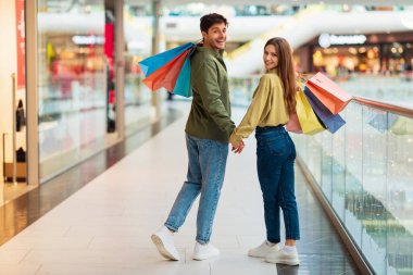 Alışveriş yapan çift alışveriş merkezinde el ele tutuşup çanta taşıyor.