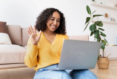 Neşeli genç Afrikalı Amerikalı kadın dizüstü bilgisayarından web kamerasına el sallıyor.