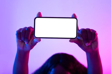 Tanımlanamayan genç Afrikalı Amerikalı kadın kafasının üstünde boş akıllı telefon tutuyor. Neon ışıklarıyla, yakın plan.
