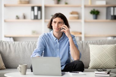 Bilgisayar sorunları. Akıllı telefondan konuşan, dizüstü bilgisayar kullanan müşteri yardım hattını arayan hoşnutsuz genç adam.