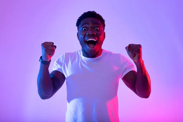 Nadšený mladý afroameričan křičí WOW, gestikuluje ANO, dosahuje úspěchu v neonovém světle — Stock fotografie