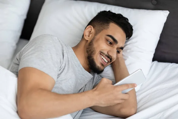 Primer plano de hombre árabe guapo descansando en la cama con Smartphone — Foto de Stock