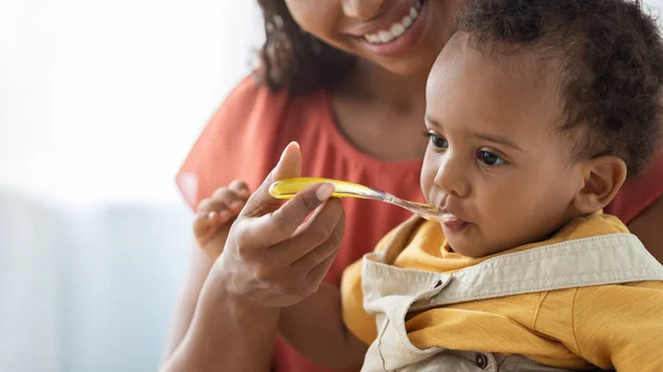 Συνήθειες βρεφικής διατροφής. Χαμογελώντας μαύρη μητέρα ταΐζοντας χαριτωμένο βρέφος από το κουτάλι — Φωτογραφία Αρχείου