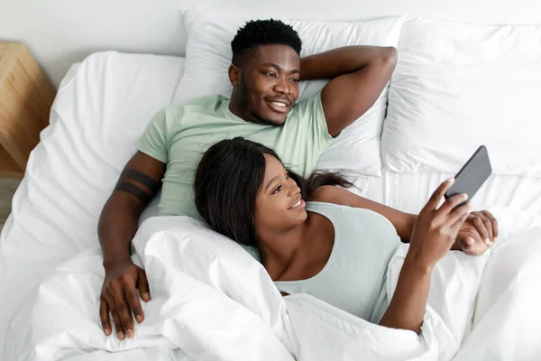 Χαρούμενη ελκυστική χιλιετή αφροαμερικανός άνδρας και η κυρία ξυπνήσει το πρωί ρολόι βίντεο στο smartphone — Φωτογραφία Αρχείου