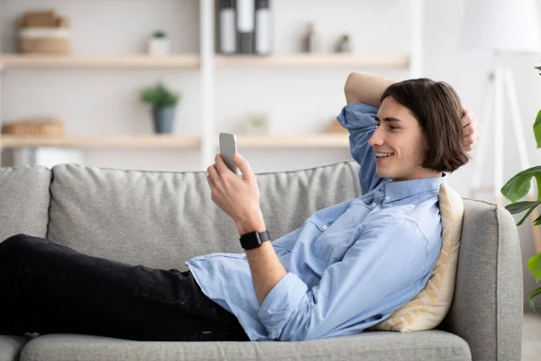 放松的男人躺在沙发上，用智能手机，和女朋友聊天，或者查社交媒体，自由自在的空间 — 图库照片