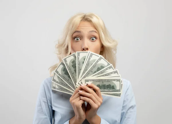 Σοκαρισμένη επιχειρηματίας καλύπτει το πρόσωπό της με χρήματα, κρύβεται πρόσωπο πίσω από δολάριο ανεμιστήρα μετρητών στα χέρια της, φως φόντο — Φωτογραφία Αρχείου