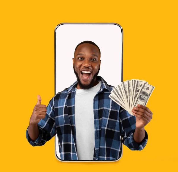 Happy millennial black guy with open mouth show many dollar on blank screen of big phone — Stok Foto