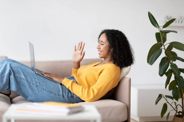 Conceito de comunicação online. Millennial mulher negra sentado no sofá, acenando na webcam, tendo vídeo chat em casa — Fotografia de Stock