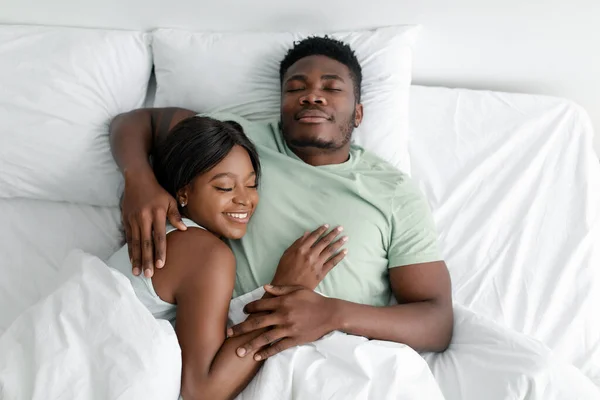 Mutlu, çekici, Afro-Amerikan erkek sarılan kadın beyaz rahat yatakta yatıyor ve birlikte yatıyorlar. — Stok fotoğraf